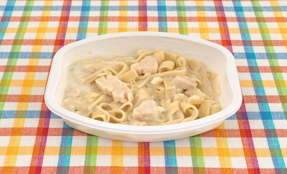 Single serving TV dinner of fettuccini with chicken on a colorful place mat.