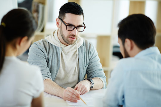 Portrait of  handsome adult man dressed in business casual discussing work with colleagues at meeting table in modern office, pointing at  documents