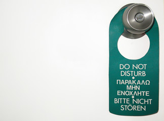 A do not disturb sign placed on a doorknob of a white door and side positioned with plenty of copy space