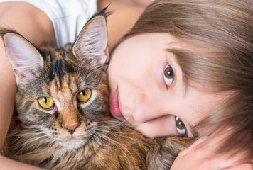 Happy little girl hugging lovely kitten. Cute ten year old child playing with her cat - close up. Portrait of beautiful kid holding on hands big fluffy Maine Coon kitty.