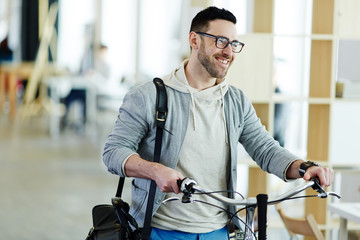 Fototapeta premium Portrait of casual contemporary business man taking bicycle to work in modern creative office