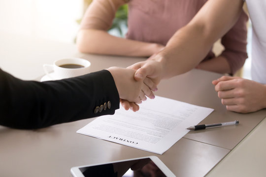 Male customer and female insurance broker shaking hands, couple and real estate agent handshaking after signing document, close up of making deal with satisfied clients, contract with a firm