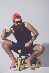 bearded angry man holds green baseball bat on bicycle toy