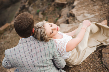 Love, romance and people concept - happy young couple hugging sitting on the edge of a cliff outdoors