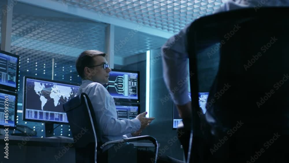 Poster Team of Technical Moderators Have Discussion in Monitoring Room. System Control Room is full of Working Displays.  Shot on RED EPIC-W 8K Helium Cinema Camera.