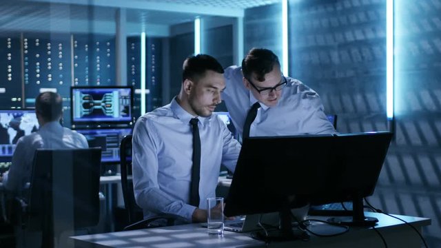 Two Operation Engineers Working on Solving Problems in System Control Room. In the Background Their Colleague, Displays and Server Racks.  Shot on RED EPIC-W 8K Helium Cinema Camera.