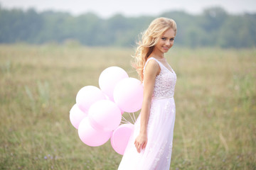 Fototapeta na wymiar Beautiful young girl in pink dress with balloons in hands on nature background in summer