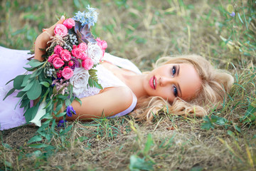 Fototapeta premium Beautiful young girl lying down with bouquet of fresh flowers on nature