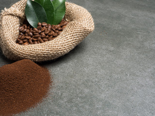Coffee sack with roasted beans and pile of grounded coffee over dark gray granite plate