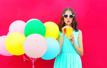 Obraz na płótnie Canvas Happy woman drinks a fruit juice from cup with an air colorful balloons over a pink background