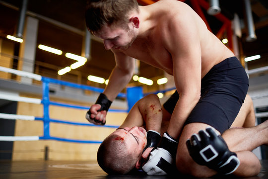 Portrait of professional wrestlers fighting in boxing ring: man hitting bloody opponent in face tackling him to floor