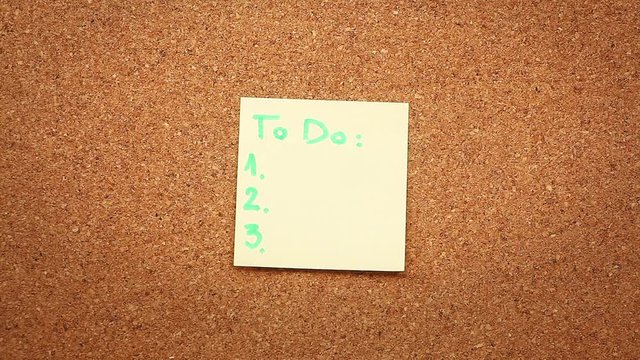 Close up footage of a person sticking a to do list on a cork board.