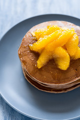 Traditional breakfast: stack of pancakes with orange slices and sweet sauce on blue wooden table. Selective focus