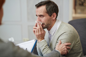 Naklejka premium Man addicted to alcohol wiping tears during conversation with psychologist
