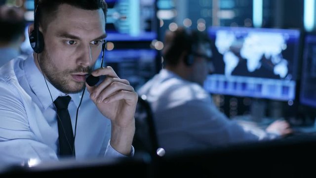 In Monitoring Room Technical Support Specialist Speaks into Headset. His Colleagues are Working in the Background  Shot on RED EPIC-W 8K Helium Cinema Camera.