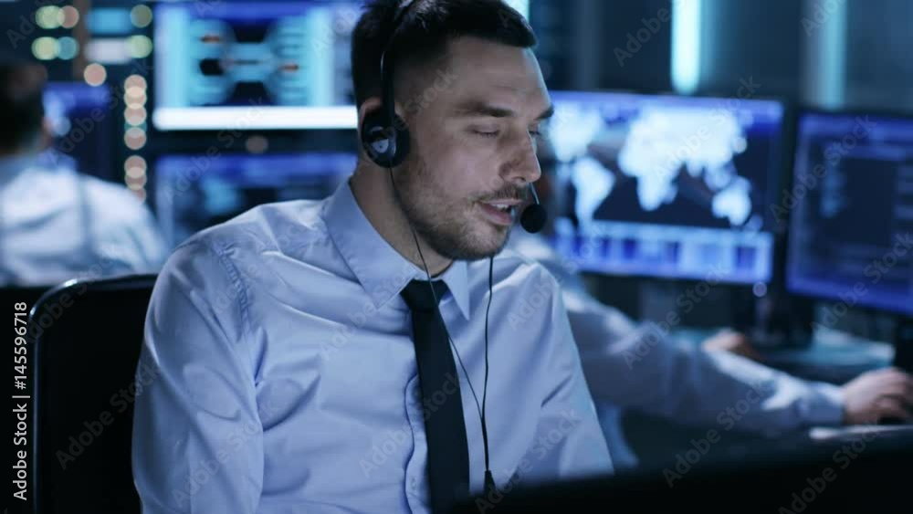 Poster in system control center technical support specialist speaks into headset. his colleagues are workin