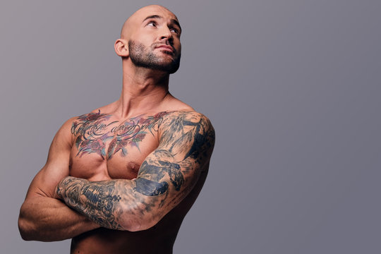 Portrait of shaved head, muscular male with crossed arms and tattoos on his  body.