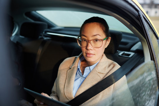 Female broker with gadget looking at camera through cab window