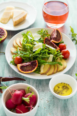 Fresh spring salad with arugula, pear and orange slices and walnuts on wooden table. Selective focus
