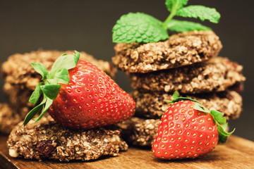 Brown oatmeal cookies with red strawberry on a wooden chopping board
