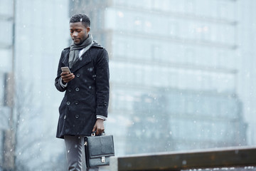 Man with smartphone and briefcase in snowfall