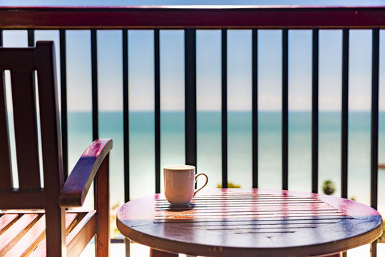 coffee cup on wooden table and chair at balcony with sea view ,concept of relaxing and vacation