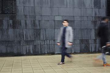 Hurrying men walking down trottoire along black wall of modern building