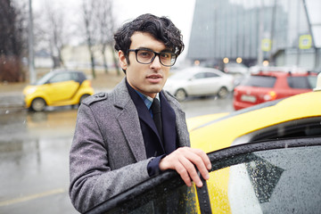 Young man in eyeglasses going to get into taxi cab