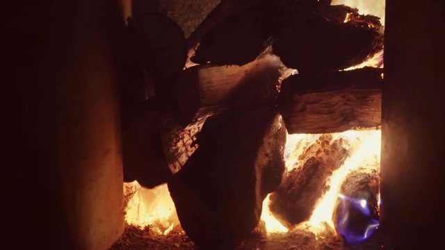 A large pile of firewood, burning in a brick fireplace, the flames of flame burst up, real firewood, very warm. 4 k video