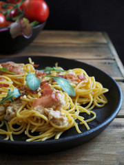 Spaghetti carbonara in black pan and fresh tomatoes on wooden table.