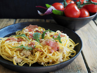 Spaghetti carborana in black pan and fresh tomatoes on wooden table.