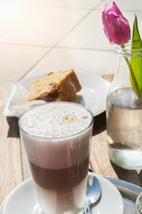 Latte, pie and flower on a table in the sunlight