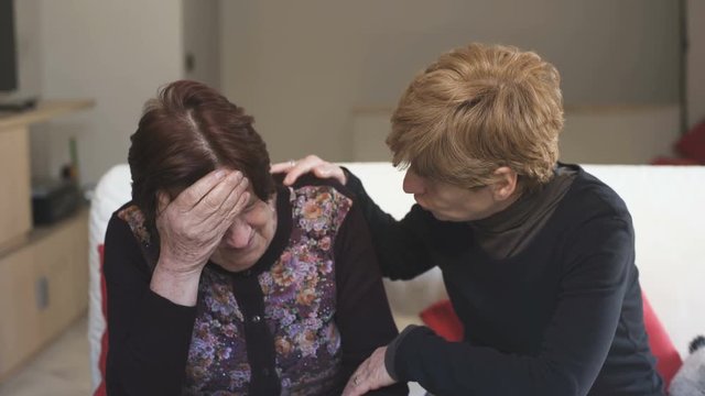 Daughter consoles the old sad mother crying sitting on the couch