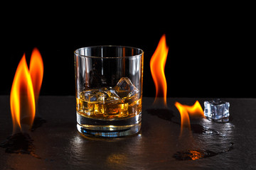 glass of whiskey with ice on a background of a burning flame