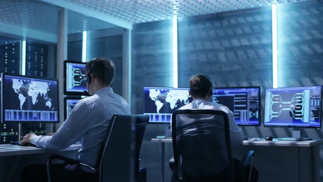 Panorama Shot of System Control Room with Three Technical Controllers Working at Their Workstations With Multiple Displays. Shot on RED EPIC-W 8K Helium Cinema Camera.