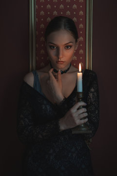 Beautiful and sad woman in a dark room with a candle.