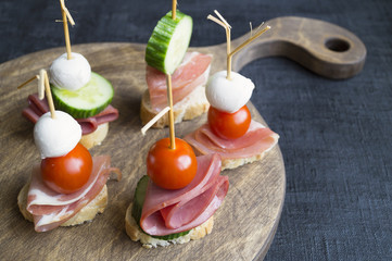 canapés with ham and tomatoes on wooden Board
