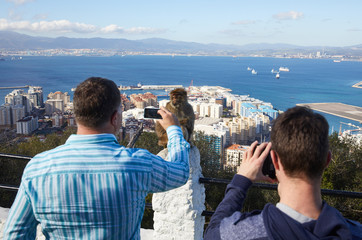 Gibraltar, Affenfelsen, Touristen fotografieren einen Berberaffen,  dahinter die Meerenge von...
