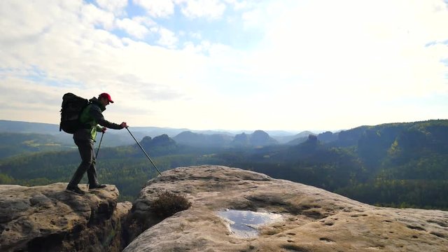 Tall tourist guide looking in paper  map. Hiker is  hiking with trekking poles and heavy backpack.  Man hiker on the rocky edge check the position in the map.  Wild hilly nature park.