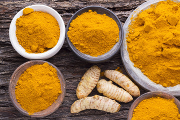 Turmeric powder and roots on wooden background



