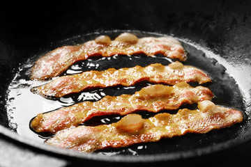 Strips of bacon cooking on pan, closeup