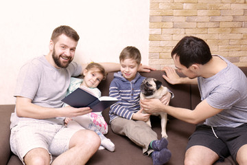 Male gay couple with children sitting on sofa at home