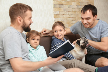 Male gay couple with children sitting on sofa at home