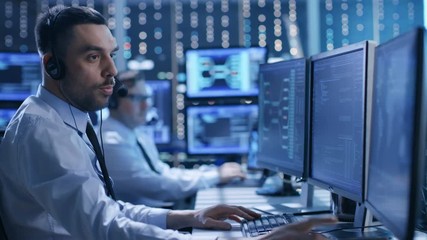 In the System Control Center Technical Support Team Gives Instructions with the Help of the Headsets. Room is Full of Displays with Various Data on them. Shot on RED EPIC-W 8K Helium Cinema Camera. - Powered by Adobe