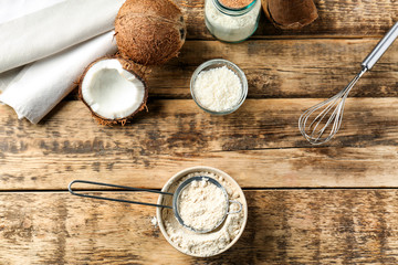 Bowl with coconut flour and sieve on wooden background
