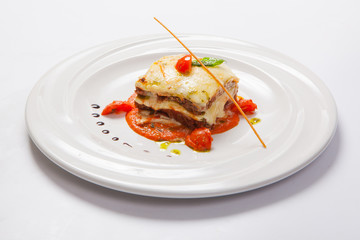 Lasagna on a white plate with herb and tomato sauce