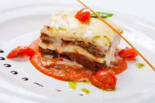 Lasagna on a white plate with herb and tomato sauce