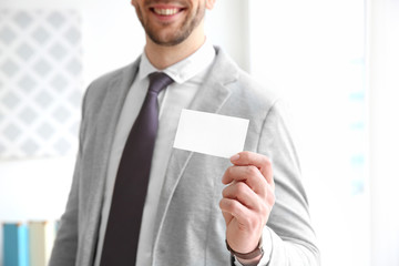 Handsome young man with business card on blurred background, closeup