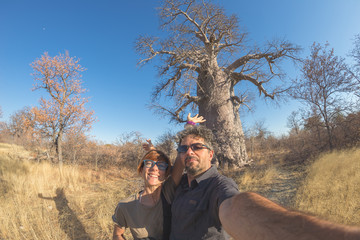 Couple taking selfie near Baobab plant in the african savannah with clear blue sky. Fisheye view from below, toned image. Wilderness safari and adventure in Africa. © fabio lamanna
