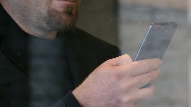 close up on bearded man typing on smartphone behind a glass window